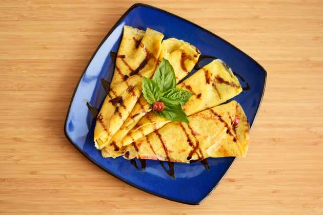 4 rolled savoury crepes with drizzled balsamic reduction and basil garnish