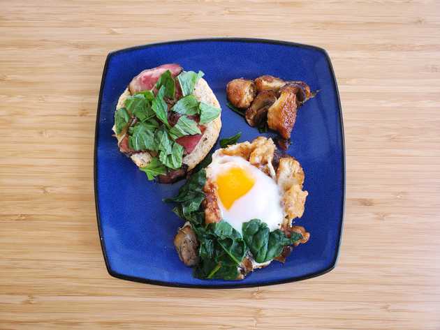 Open face breakfast sandwich with egg, prosciutto, greens, and other toppings