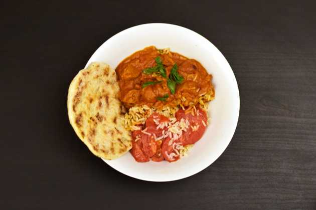 Rice topped with "butter chicken", tomatoes, and a side of flatbread