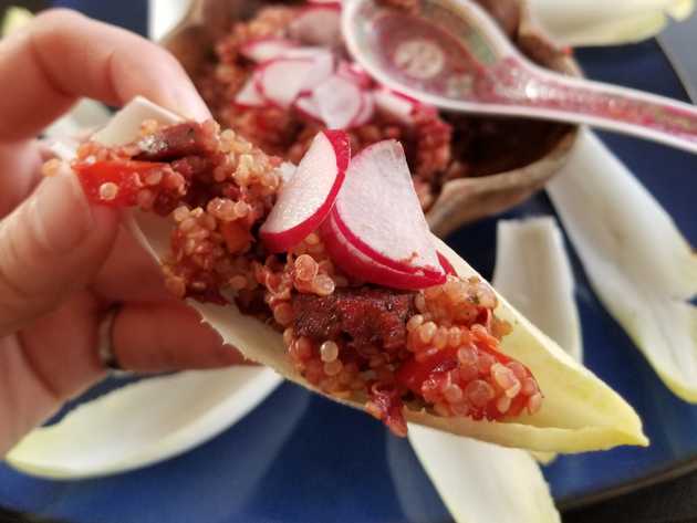 Endive boat topped with grain mix, sliced sausage, and fresh radishes